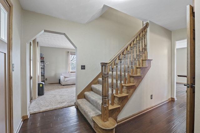stairs featuring baseboards, arched walkways, and wood-type flooring