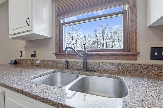 room details featuring white cabinetry, light stone countertops, and a sink