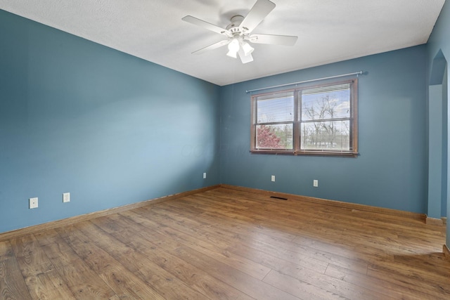 empty room featuring wood finished floors, visible vents, a ceiling fan, and baseboards
