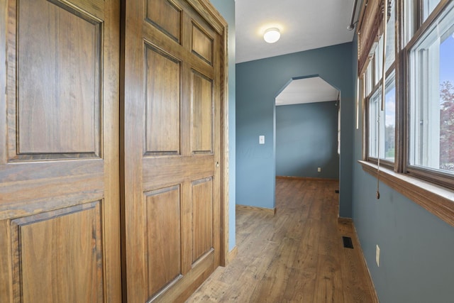 corridor with arched walkways, light wood-style flooring, a healthy amount of sunlight, and baseboards