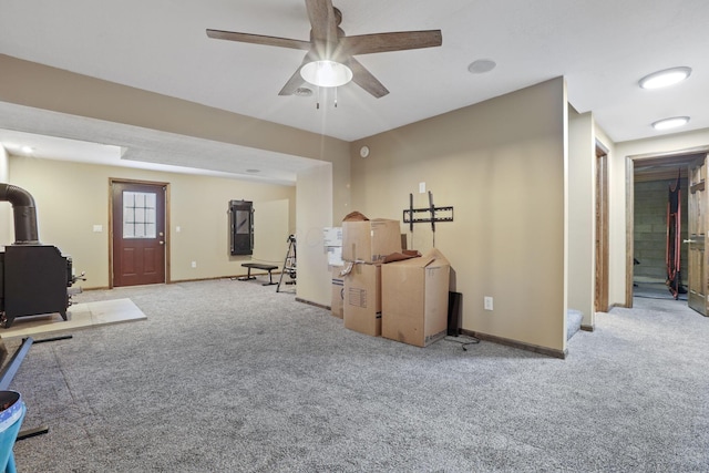 interior space featuring a wood stove, carpet flooring, baseboards, and a ceiling fan