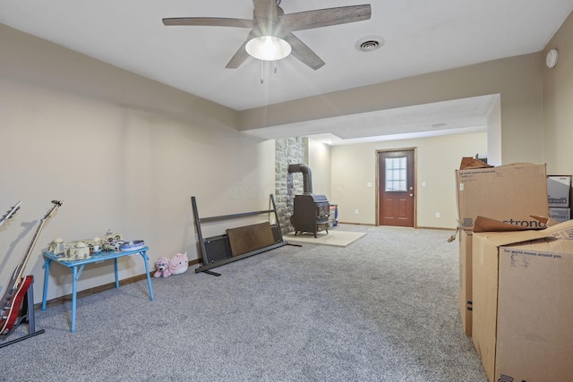 rec room featuring ceiling fan, carpet floors, a wood stove, baseboards, and visible vents