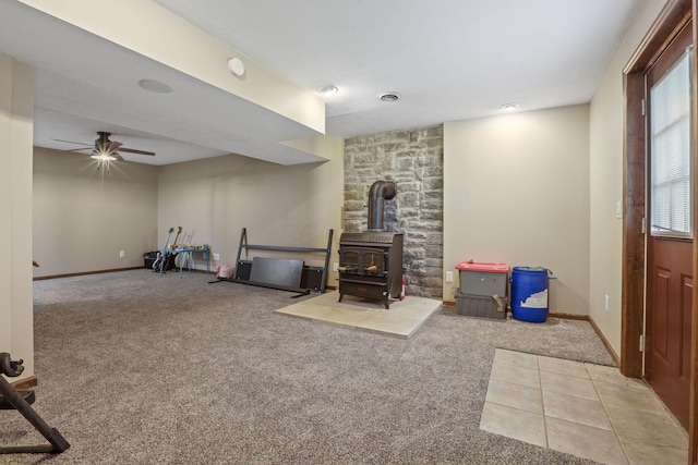 interior space featuring a wood stove, baseboards, carpet flooring, and ceiling fan