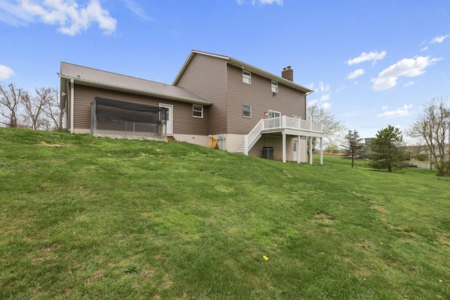 rear view of property with a chimney, a deck, stairs, a yard, and metal roof