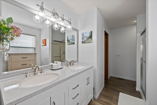 bathroom with double vanity, a sink, wood finished floors, and a shower stall