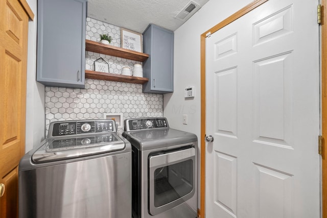 laundry area with a textured ceiling, visible vents, cabinet space, and washing machine and clothes dryer