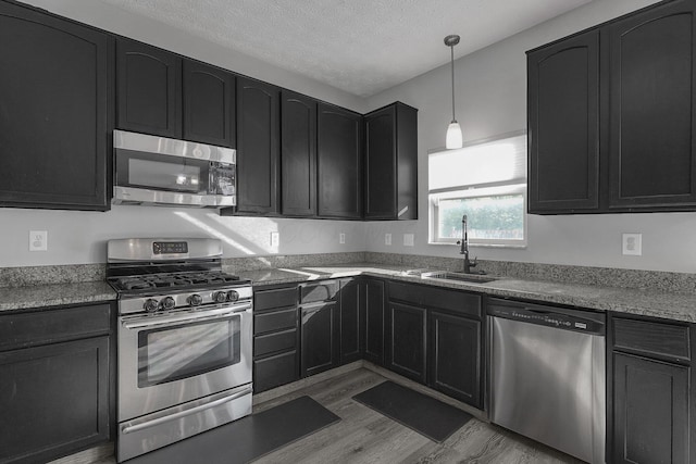 1065 Mastell Dr, Reynoldsburg, OH 43068 - kitchen with stainless steel appliances, a sink, light wood-style flooring, dark cabinets, and a textured ceiling