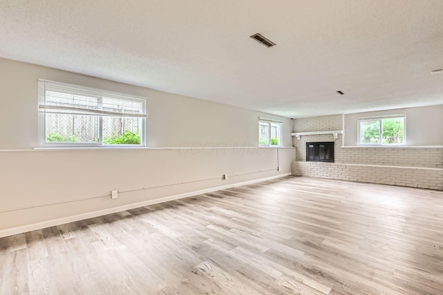 unfurnished living room featuring healthy amount of natural light, wood finished floors, brick wall, a fireplace, and baseboards