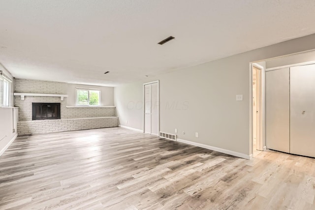 unfurnished living room with light wood-style floors, brick wall, a fireplace, and baseboards