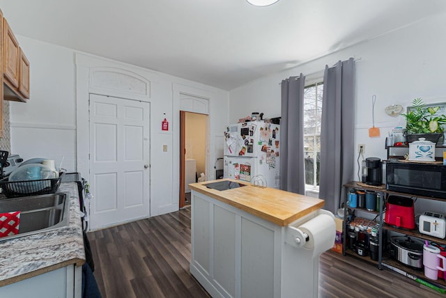 kitchen with black microwave, freestanding refrigerator, dark wood-style floors, and wooden counters