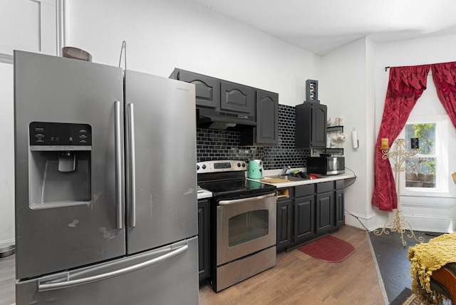kitchen featuring light wood finished floors, under cabinet range hood, stainless steel appliances, light countertops, and decorative backsplash