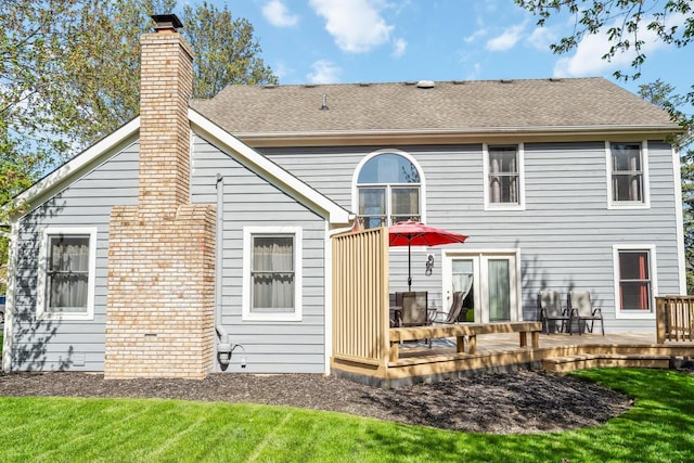 back of property featuring a lawn, a shingled roof, a wooden deck, and a chimney