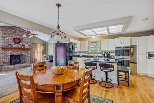 dining room featuring a fireplace, a ceiling fan, vaulted ceiling, and light wood-style floors