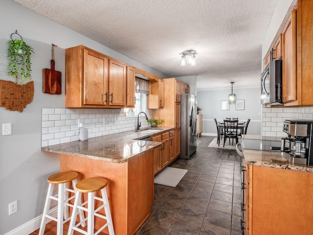 kitchen featuring stainless steel appliances, a peninsula, a sink, backsplash, and a kitchen bar