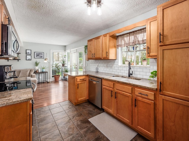 kitchen featuring a textured ceiling, a sink, decorative backsplash, stainless steel appliances, and a peninsula