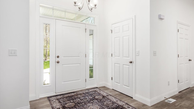 foyer entrance with an inviting chandelier, wood finished floors, visible vents, and baseboards