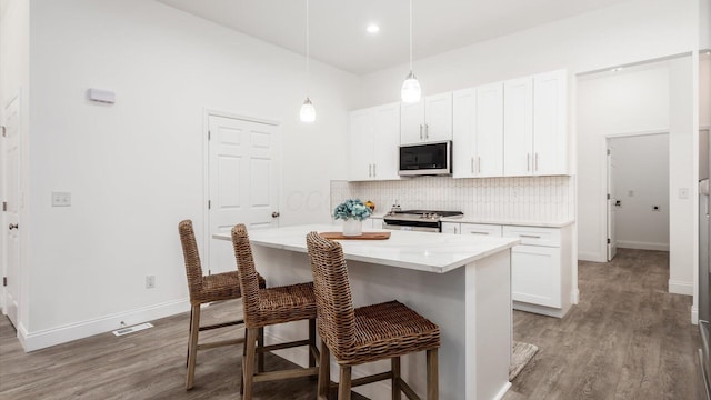 kitchen featuring decorative backsplash, a breakfast bar, stainless steel appliances, light wood finished floors, and white cabinetry