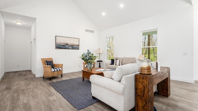 living area with high vaulted ceiling, light wood-type flooring, visible vents, and baseboards