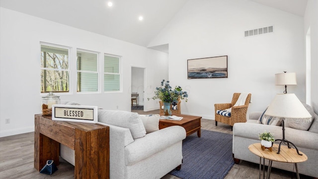living room featuring baseboards, wood finished floors, visible vents, and high vaulted ceiling