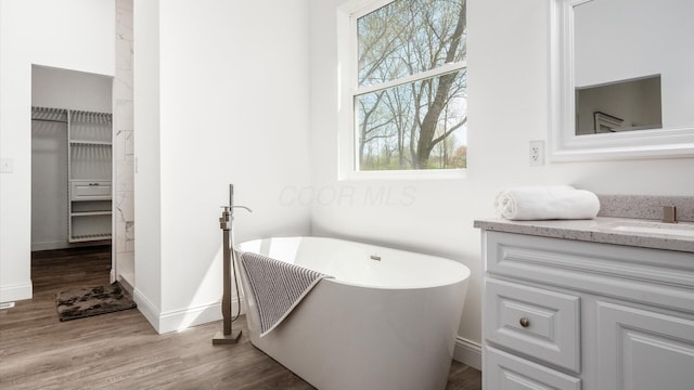 bathroom featuring baseboards, a soaking tub, vanity, and wood finished floors