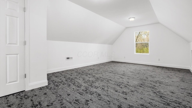 additional living space with vaulted ceiling, dark colored carpet, visible vents, and baseboards
