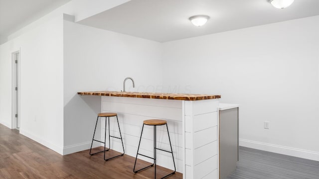 bar featuring baseboards, wood finished floors, and a sink