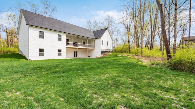 back of property with a yard, a shingled roof, and a balcony