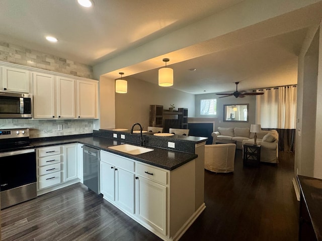 kitchen with white cabinets, a sink, stainless steel appliances, dark wood-style flooring, and a peninsula