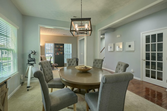 carpeted dining space with a textured ceiling, a healthy amount of sunlight, baseboards, a notable chandelier, and stairs