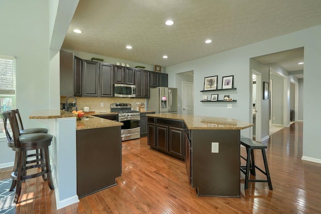 kitchen featuring stainless steel appliances, backsplash, a sink, wood-type flooring, and a breakfast bar area