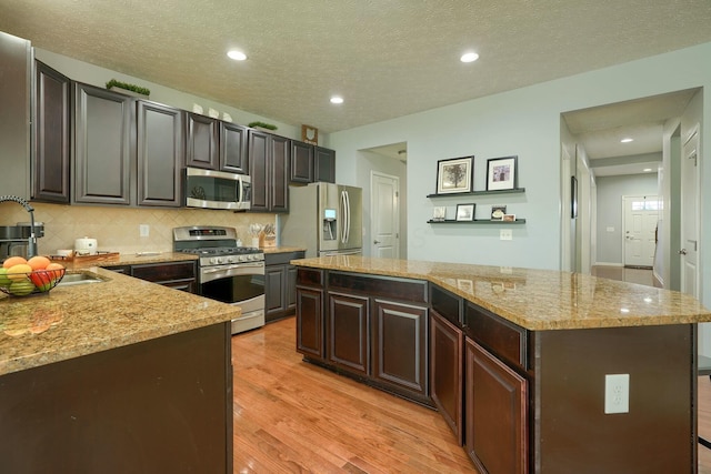 kitchen with stainless steel appliances, a center island, tasteful backsplash, light wood-type flooring, and light stone counters