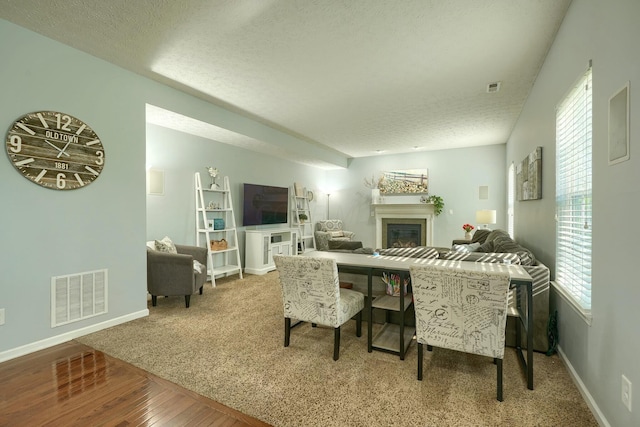 dining space with a textured ceiling, wood finished floors, visible vents, and a glass covered fireplace