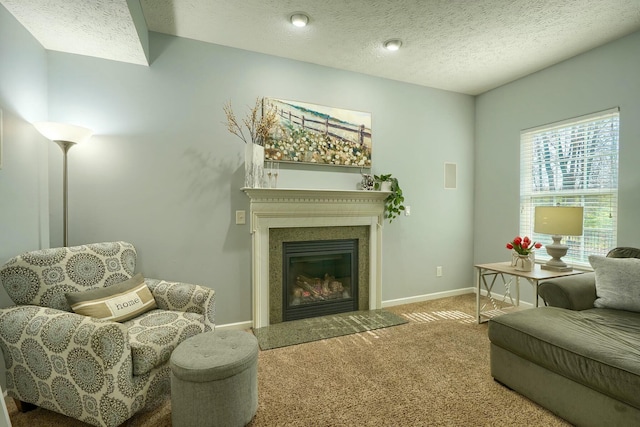 living area with a glass covered fireplace, baseboards, carpet flooring, and a textured ceiling