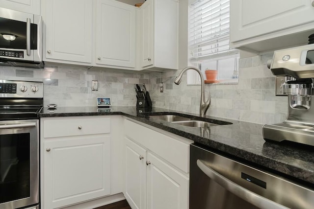 kitchen featuring dark stone counters, a sink, decorative backsplash, stainless steel appliances, and white cabinets