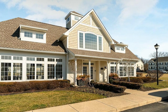 view of front facade with a shingled roof, a front lawn, and covered porch