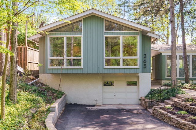 view of side of property with an attached garage, aphalt driveway, and fence