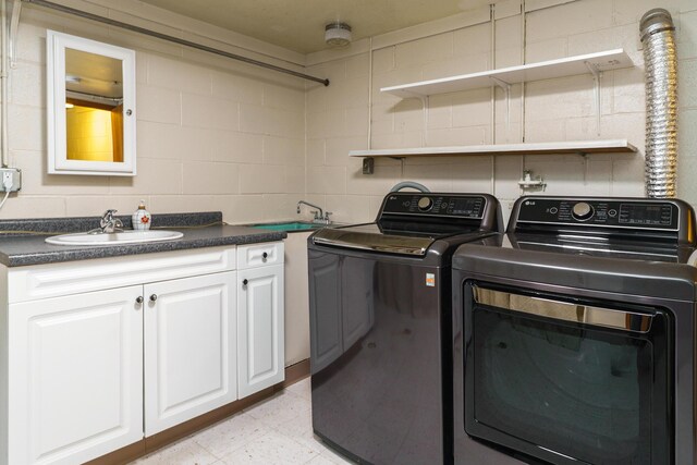 laundry room with washing machine and clothes dryer, concrete block wall, cabinet space, and a sink