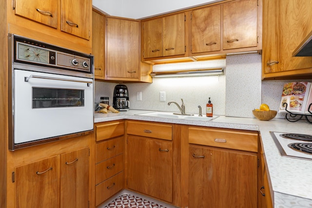 kitchen with electric cooktop, a sink, tasteful backsplash, white oven, and light countertops
