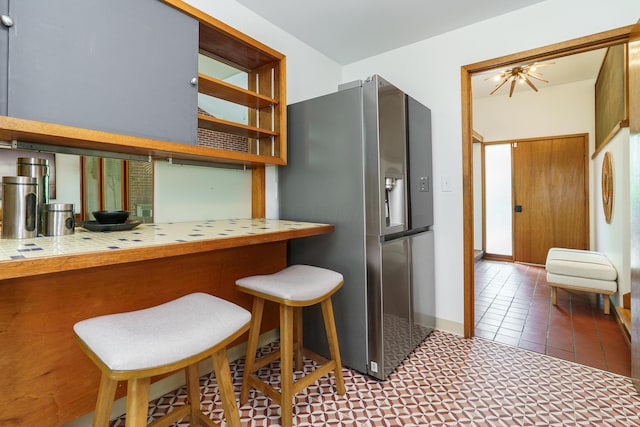 kitchen featuring a kitchen breakfast bar, stainless steel refrigerator with ice dispenser, and tile countertops