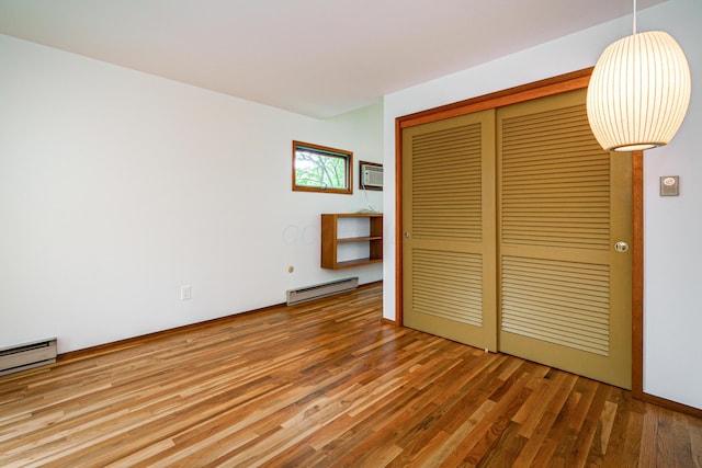 unfurnished bedroom featuring wood finished floors, a baseboard heating unit, a closet, and a baseboard radiator