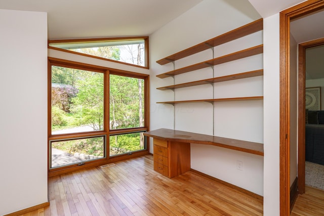 unfurnished office with built in desk, light wood finished floors, and vaulted ceiling