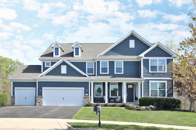 craftsman inspired home with covered porch, a shingled roof, driveway, a front lawn, and an attached garage