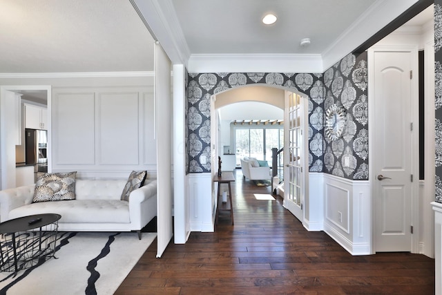 hallway featuring crown molding, dark wood-style floors, wallpapered walls, and arched walkways
