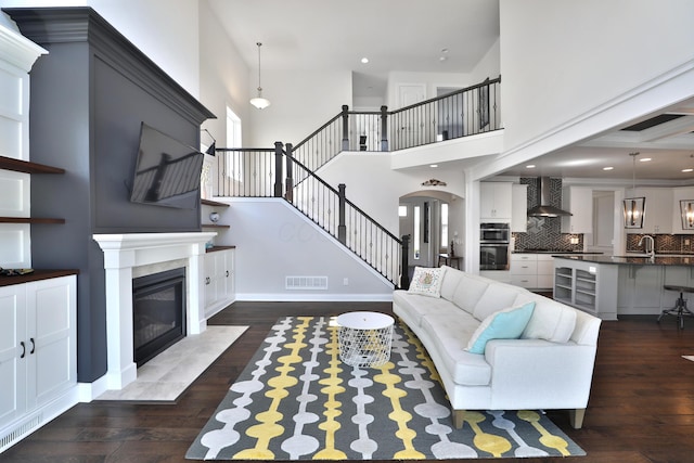 living room with a high ceiling, dark wood-style flooring, a fireplace, stairs, and visible vents