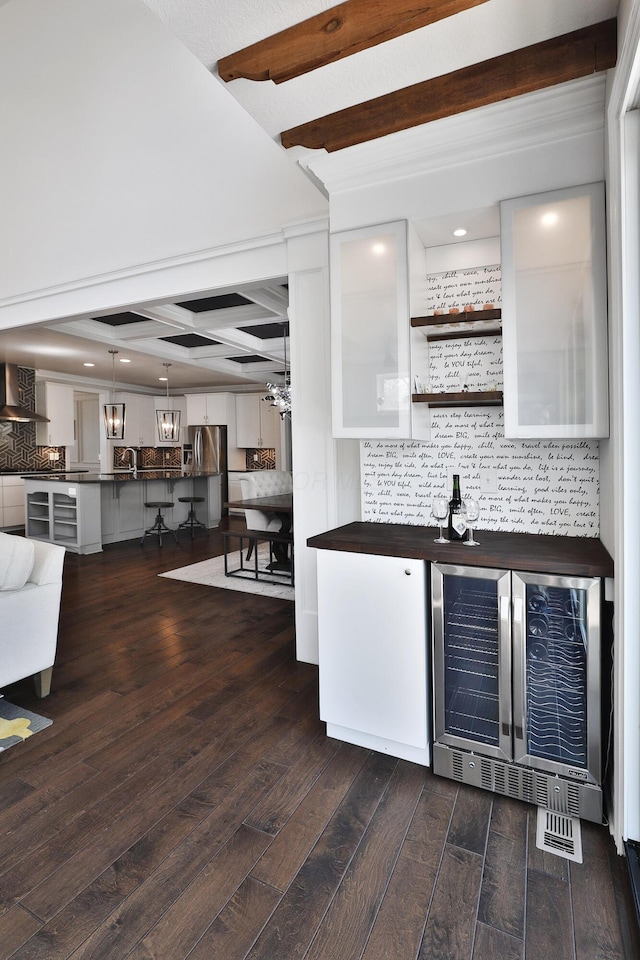 bar with dark wood-style floors, beam ceiling, wall chimney exhaust hood, backsplash, and beverage cooler