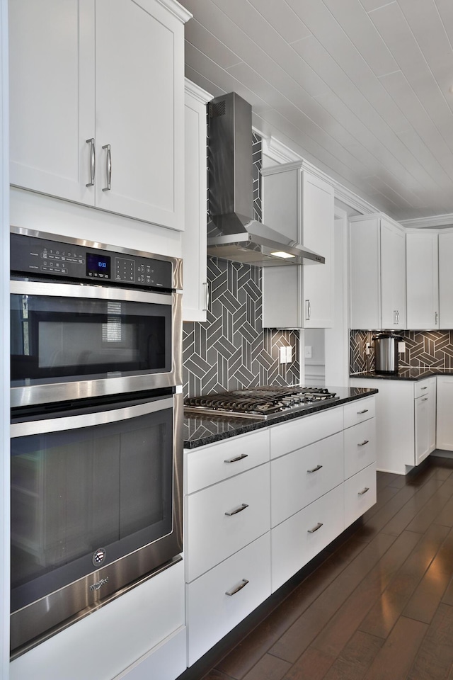 kitchen featuring wall chimney range hood, white cabinets, stainless steel appliances, dark wood finished floors, and backsplash