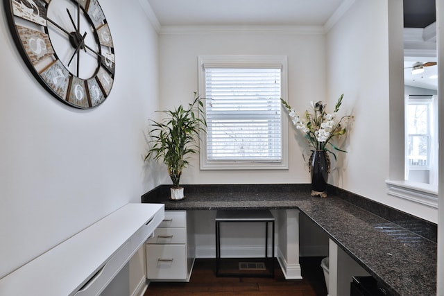 home office featuring dark wood-type flooring, ornamental molding, and built in desk