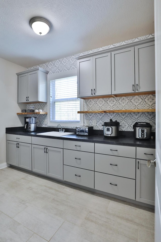 kitchen with a textured ceiling, decorative backsplash, a sink, dark countertops, and gray cabinets