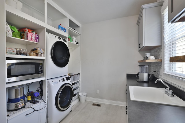 washroom featuring visible vents, stacked washer / dryer, baseboards, and a sink