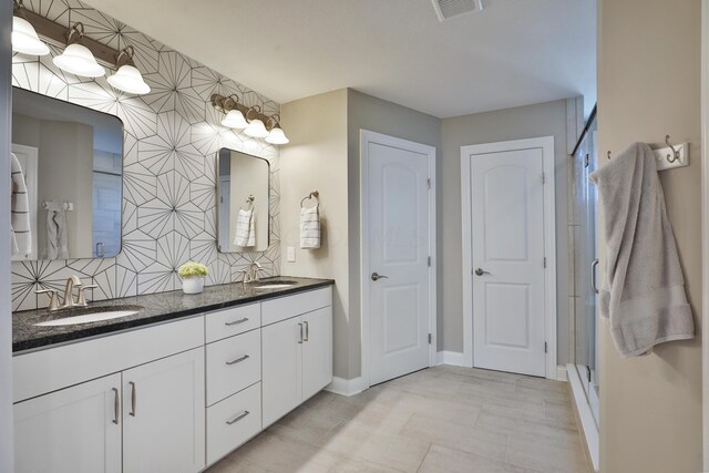 full bath with visible vents, a stall shower, double vanity, and a sink